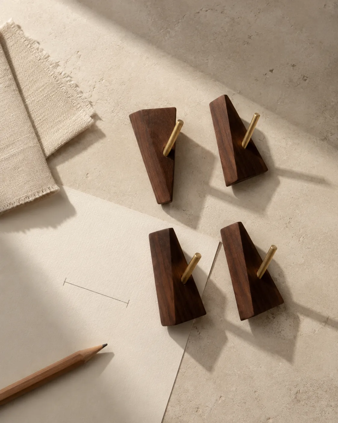 Étude de matières : quatre patères en bois et métal sur une table de pierre, avec un crayon et du lin